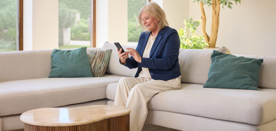 Vrouw zit thuis ontspannen en bekijkt informatie op haar mobiel dankzij persoonlijke zorg van Máxima Nova